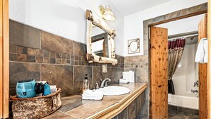 A bathroom with a stone tile backsplash, a wooden-framed mirror, a sink, and a shower area. - Relaxing Getaway Surrounded by Nature & Beauty (Duluth)