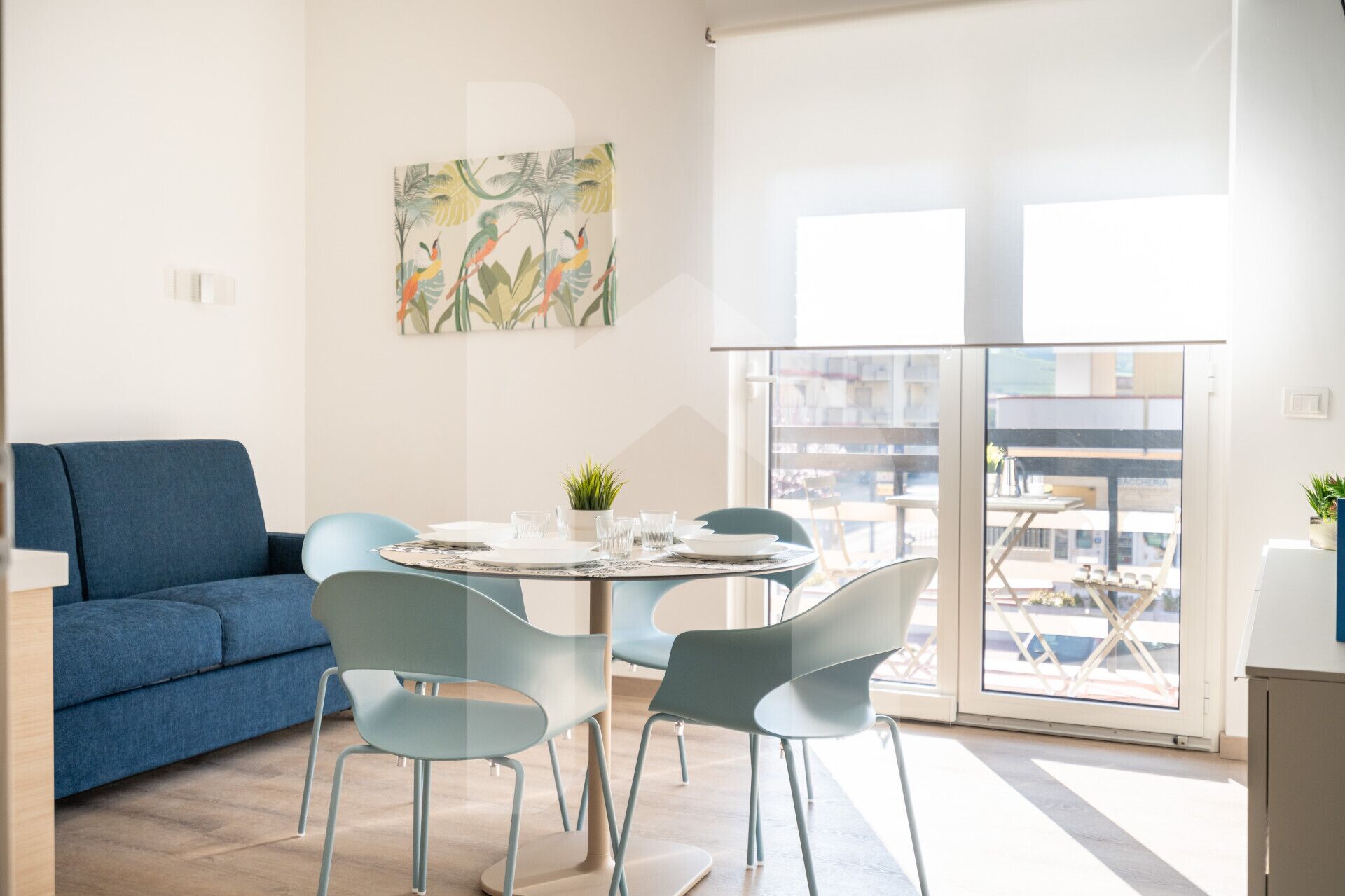 A modern living room with a blue sofa, a round table with chairs, and a large window with a city view.