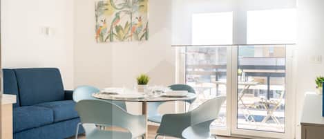 A modern living room with a blue sofa, a round table with chairs, and a large window with a view of buildings.