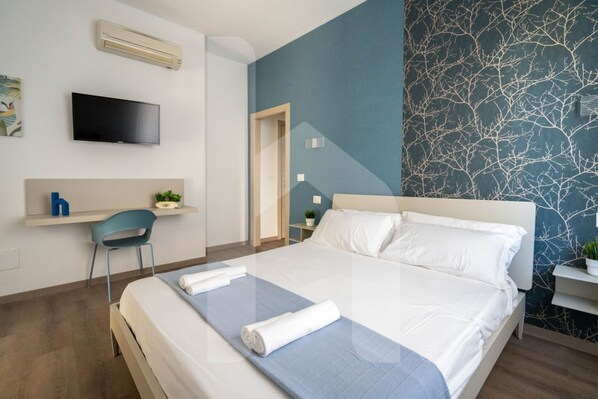 A modern hotel room with a bed, a flat-screen TV, a desk, and a chair.