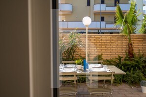 An outdoor dining area with a table set for two, surrounded by potted plants and a brick wall.