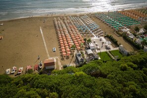A beach with rows of umbrellas and sun loungers, a pool area, and a view of the ocean.