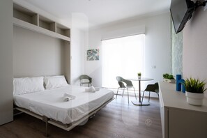 A modern hotel room with a bed, a small desk, a chair, and a window with a view.