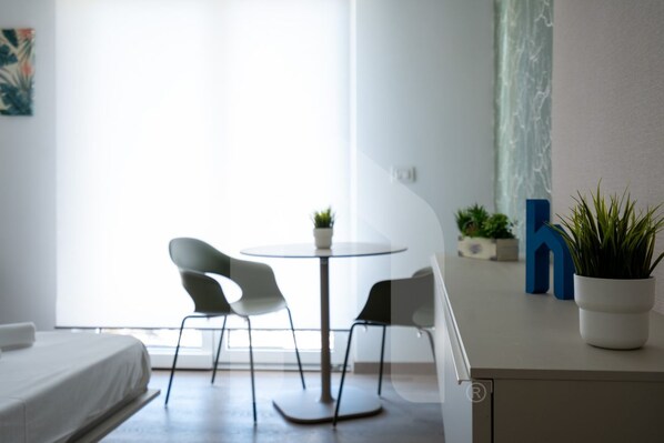 A modern room with a bed, a round table with two chairs, a potted plant, and a large window.