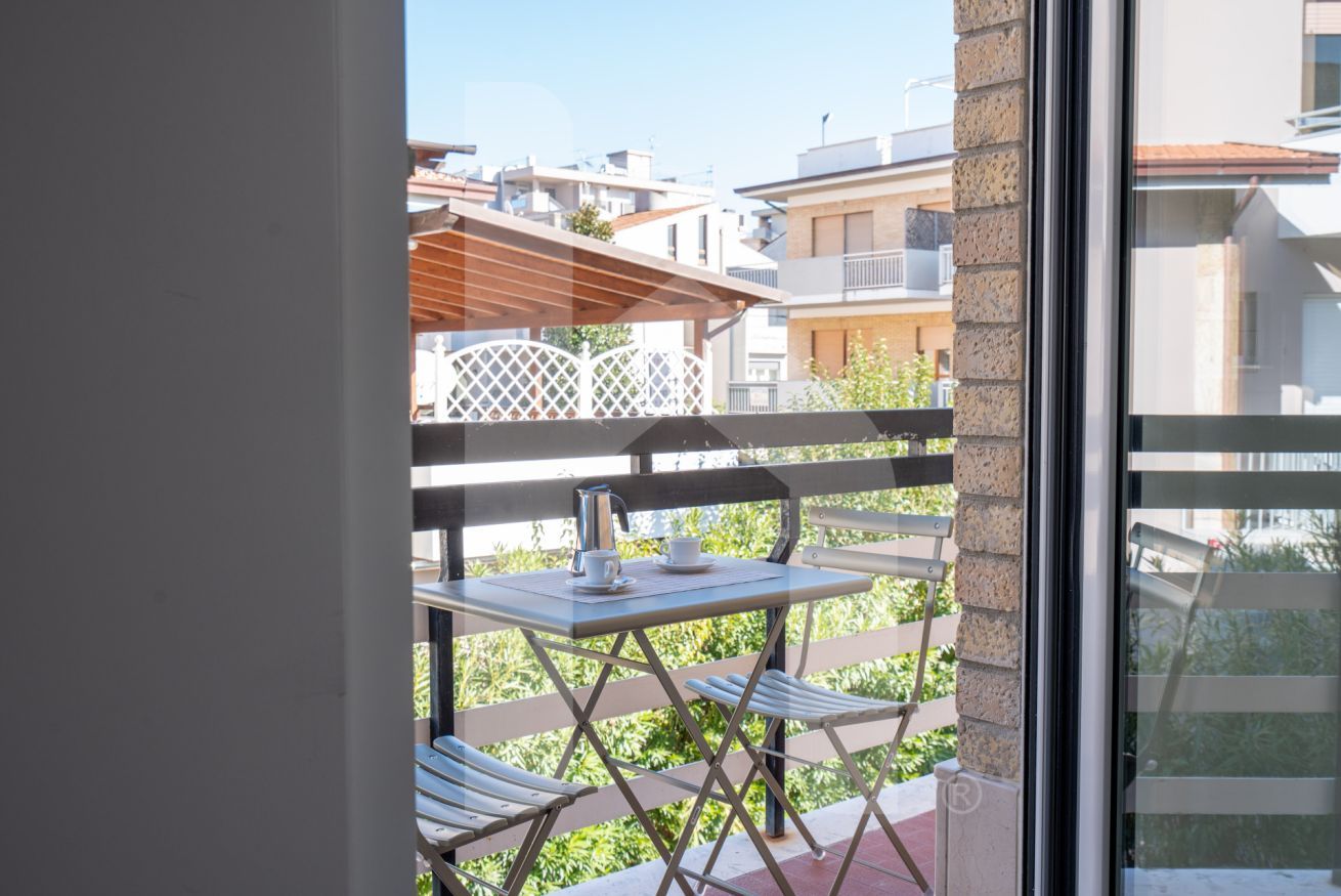 A balcony with a table and chairs, a view of neighboring buildings, and a glass door.