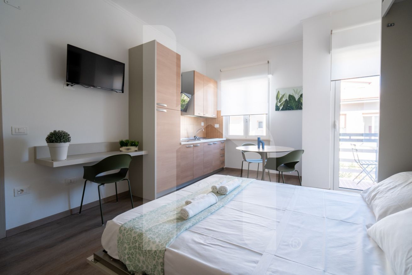 A modern hotel room with a bed, a desk, a chair, a TV, and a balcony.