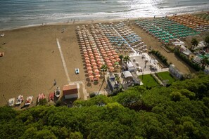 Vista aérea de una playa con hileras de sombrillas y sillas, algunas embarcaciones y un pequeño edificio.