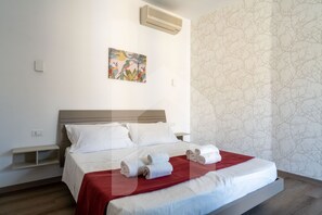 A hotel room with a bed, a wall-mounted air conditioner, a shelf, and a patterned wallpaper. - Homiday - Residence Venere, Unit 15 (Alba Adriatica)