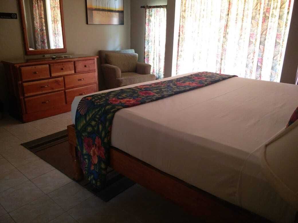 Un dormitorio con una cama, un tocador de madera, una silla y una ventana con cortinas.