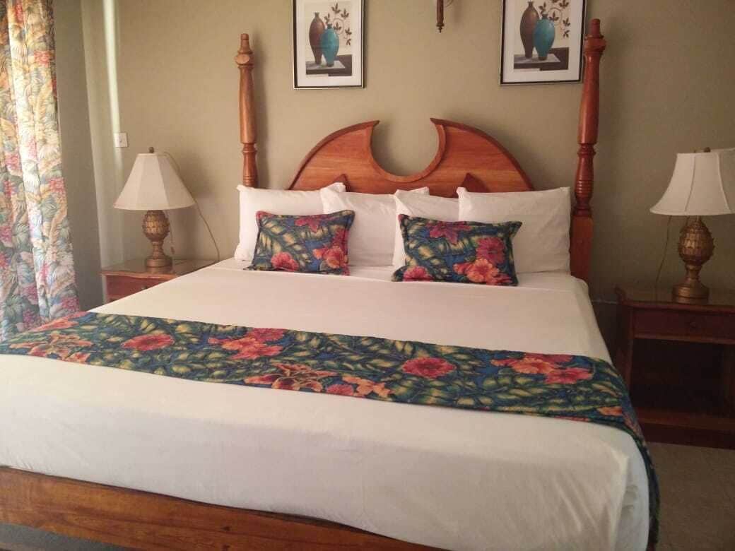 Un lit bien fait, recouvert d’une couvre-lit à motifs floraux, avec deux oreillers assortis et une tête de lit en bois. Deux lampes de chevet sont placées de chaque côté du lit.