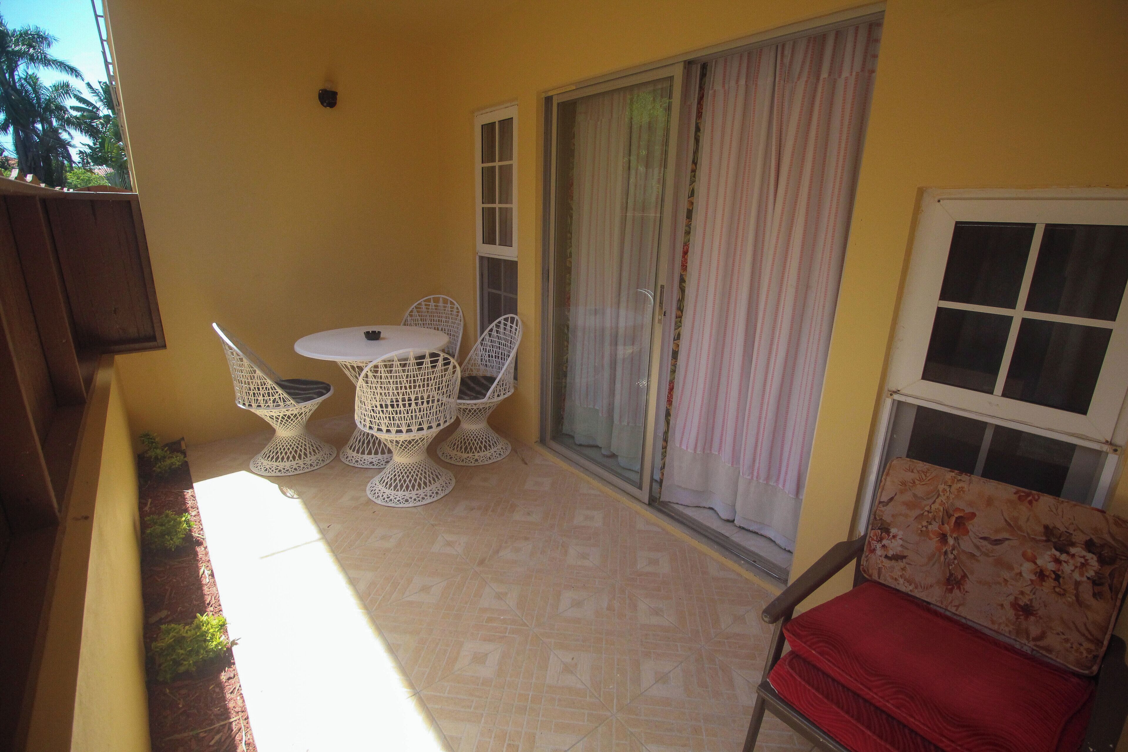 A small balcony with a table and chairs, a sliding glass door, and a window with a curtain.