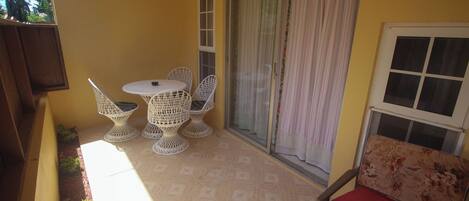A small balcony with a table and chairs, a sliding glass door, and a window with a curtain.