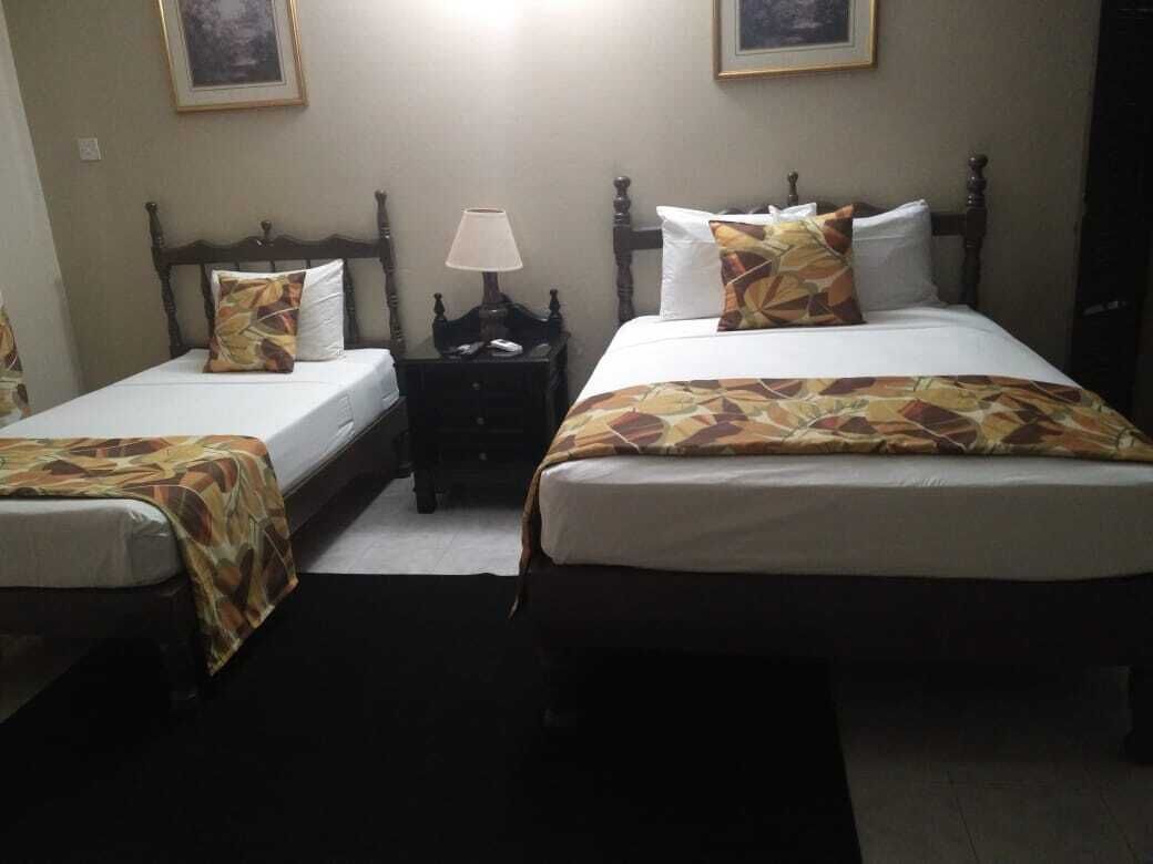 A hotel room with two single beds, each with a patterned bedspread and pillows, a nightstand with a lamp, and framed artwork on the walls.