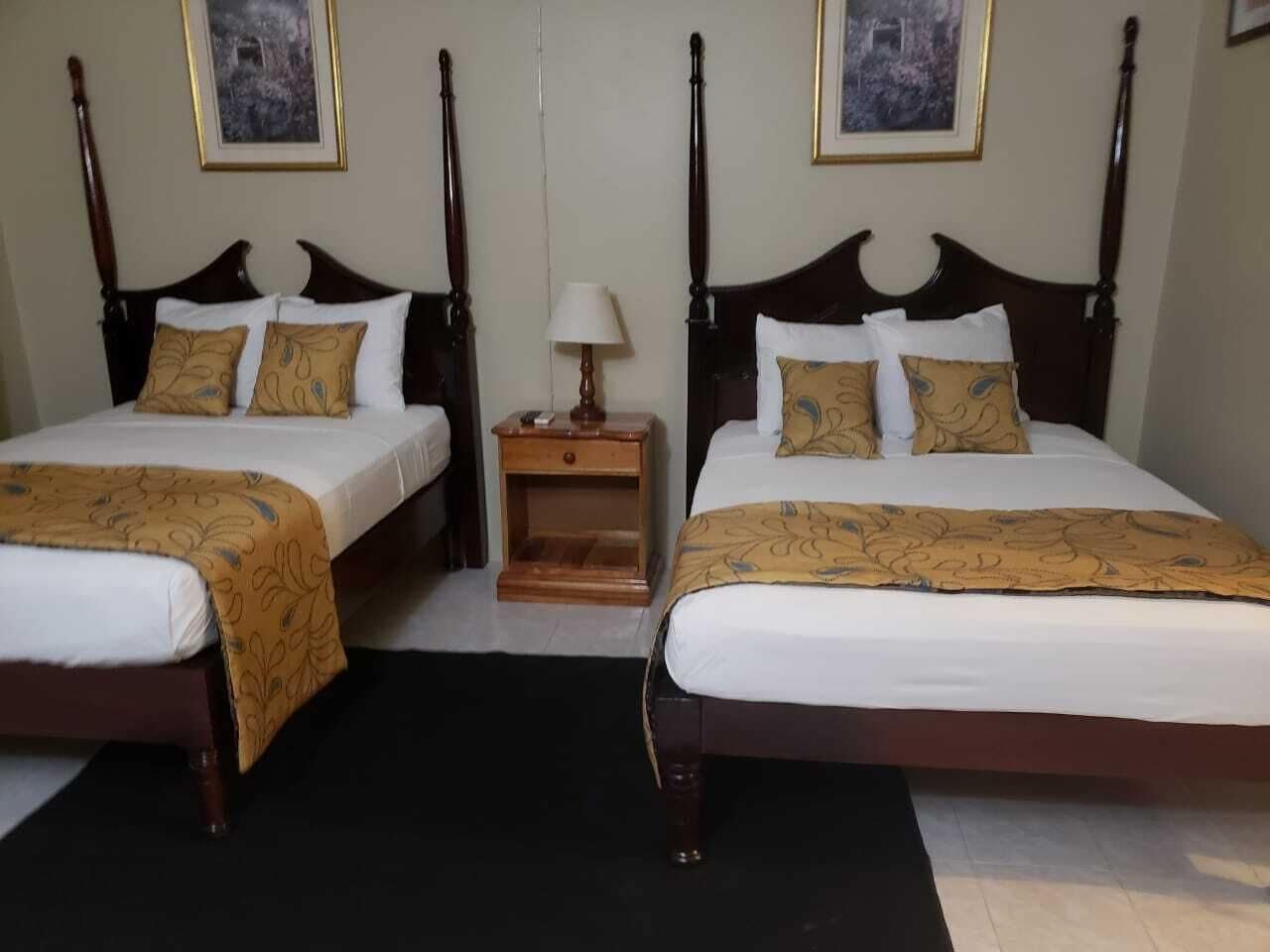 A double room with two beds, each with a wooden headboard, a nightstand, and a lamp between the beds.