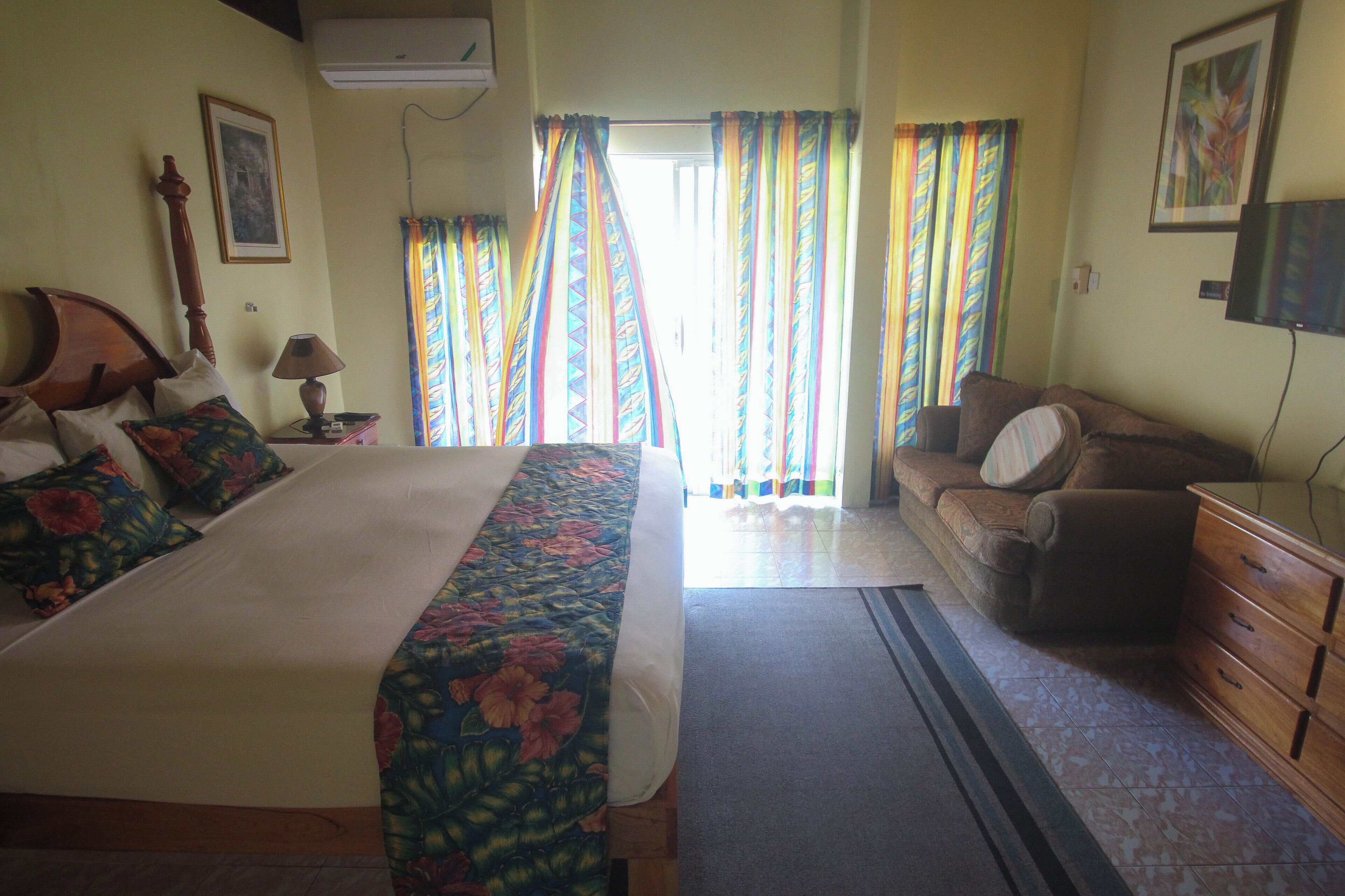 A bedroom with a bed, a sofa, a dresser, and a window with curtains.