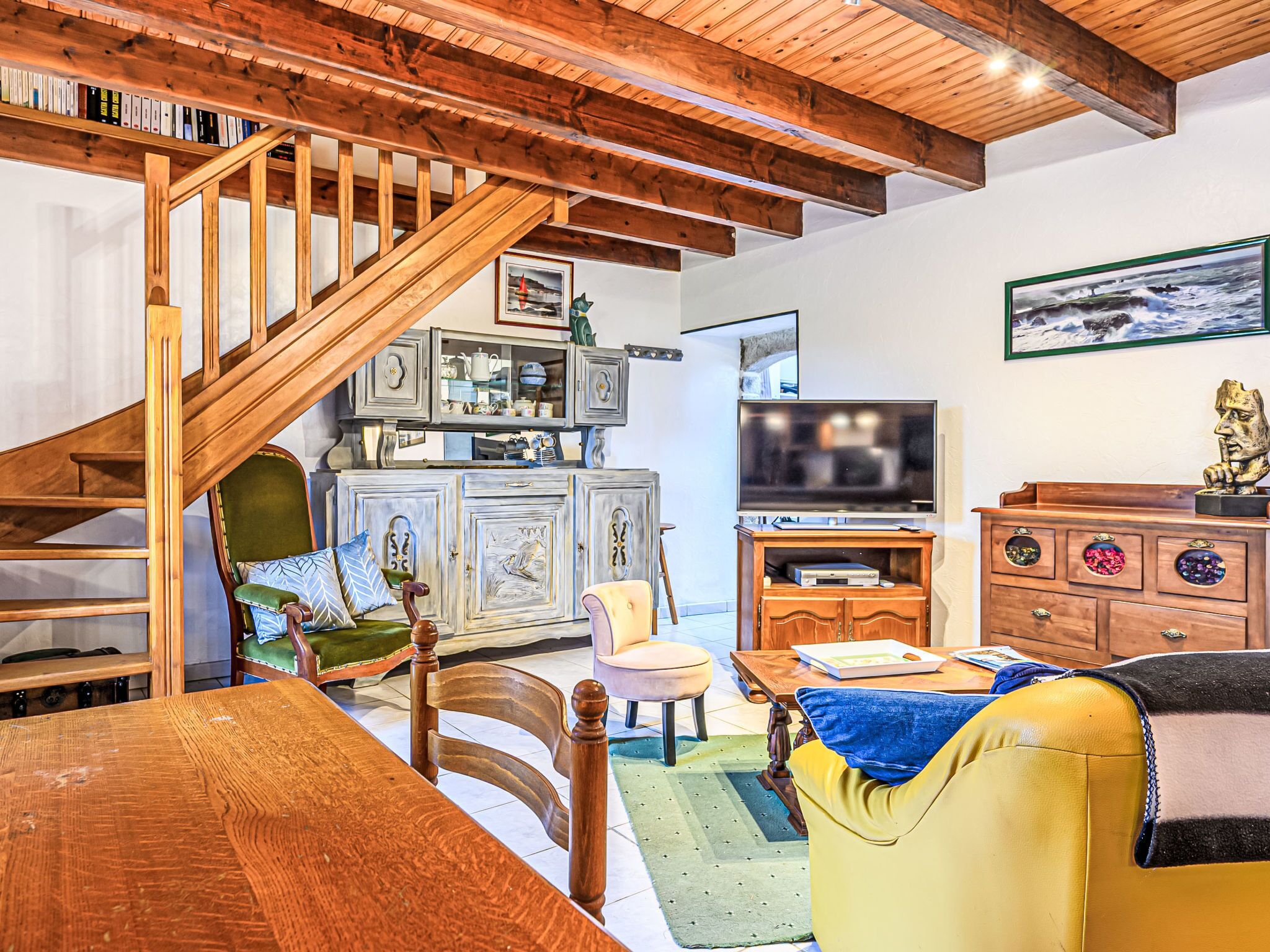 Een gezellige woonkamer met een houten trap, een televisie en een kast met decoratieve objecten.