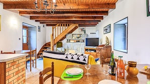 A dining area with a wooden table set for a meal, a staircase leading to an upper level, and a television in the background.