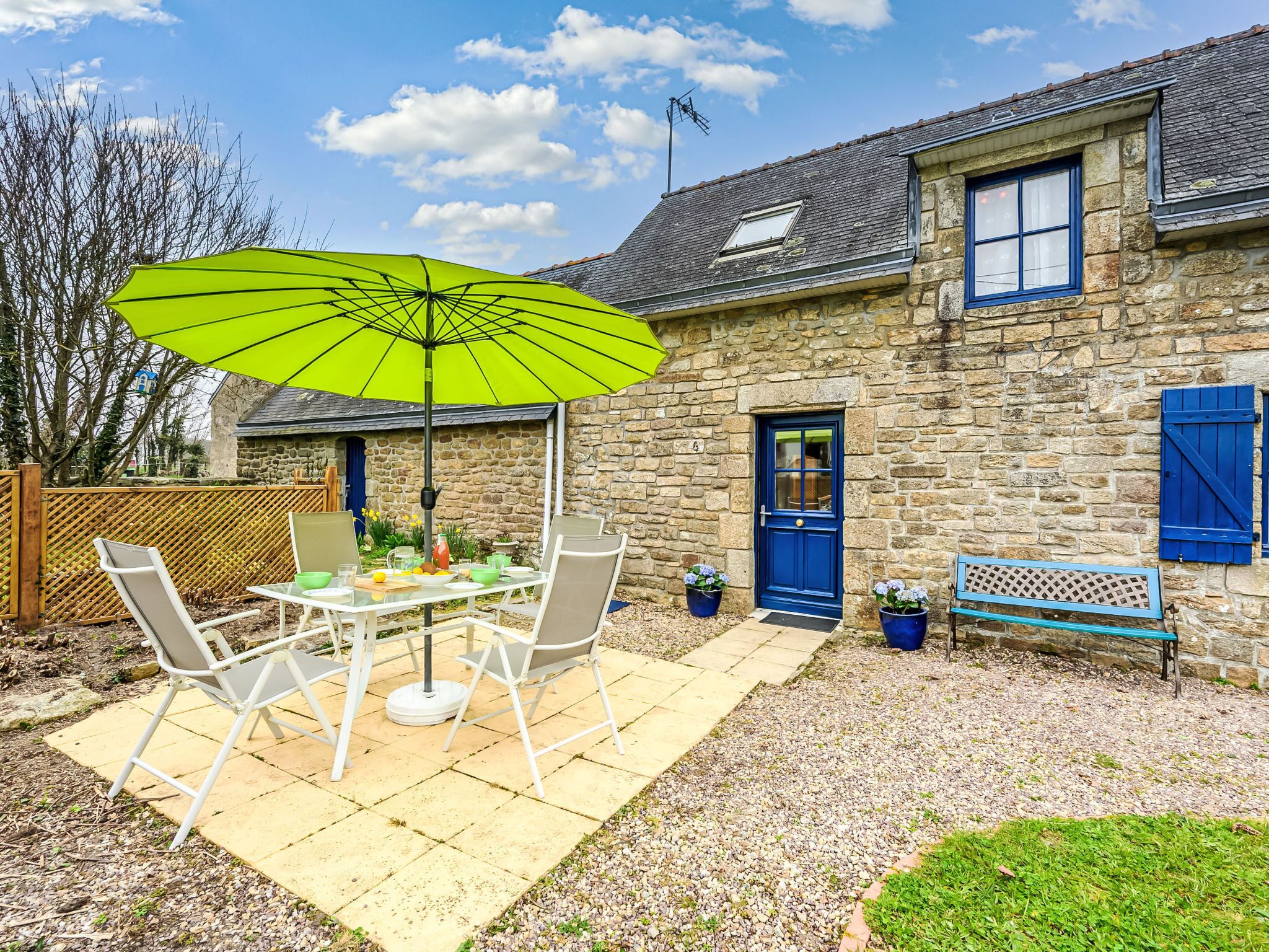 A stone house with a blue door, a patio with a table and chairs, and a bright green umbrella.