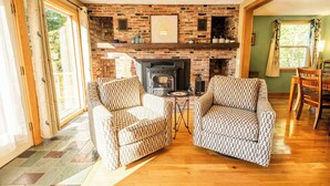A cozy living room with a brick fireplace, two patterned armchairs, and a wooden floor.