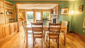 A dining area with wooden chairs and a table, a wooden bookshelf, and a view through a glass door to an outdoor space.