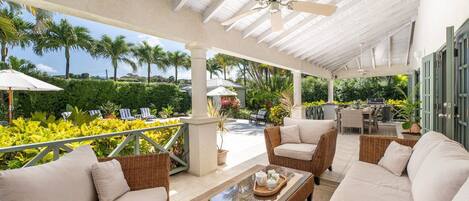 A covered outdoor seating area with wicker furniture and a ceiling fan.