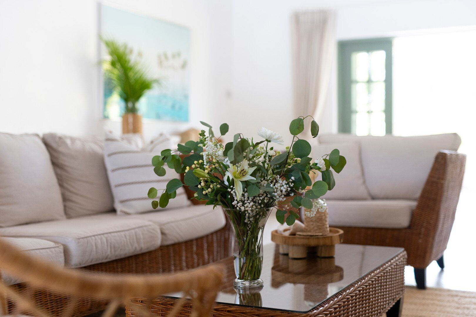 A living room with a white sofa, a glass coffee table, and a vase of flowers.