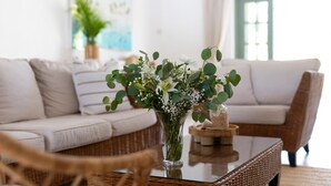 Una sala de estar con un sofá blanco, una mesa de centro de vidrio y un jarrón con flores.