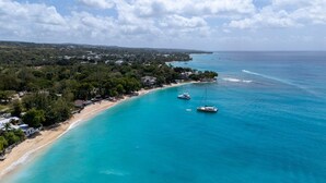 Vista aérea de una zona costera con playa, barcos y una zona boscosa densa.