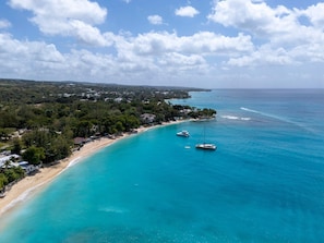 Luftaufnahme einer Küstenlandschaft mit Strand, Booten und dicht bewaldetem Gebiet.
