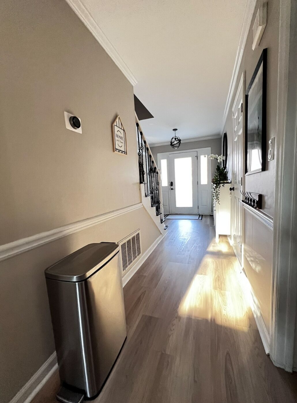 A hallway with a trash can, a staircase, and a door leading to another room.