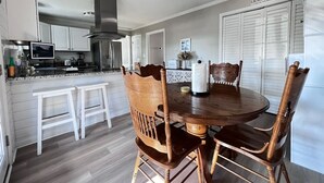 Una cocina moderna con armarios blancos, una campana extractora de acero inoxidable y un comedor con una mesa redonda de madera y cuatro sillas de madera.