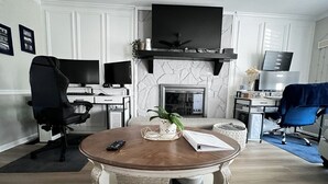 Una sala de estar con chimenea, televisor, escritorio y dos sillones.