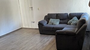 A living room with a grey sofa, a matching ottoman, and a patterned throw pillow. A white door is visible in the background. - Apartment 10 minutes from the beach (Cancún)