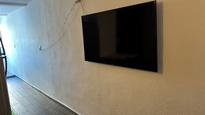 A room with a mounted flat-screen TV on a textured wall, wooden flooring, and a visible door leading to another room. - Apartment 10 minutes from the beach (Cancún)