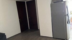 A room with a dark wooden floor, a grey refrigerator, and a grey sofa. - Apartment 10 minutes from the beach (Cancún)