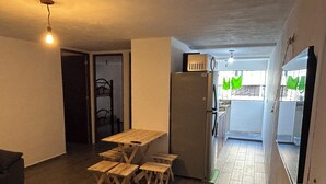 A compact kitchen with a wooden table and matching stools, a refrigerator, and a hanging light fixture. - Apartment 10 minutes from the beach (Cancún)