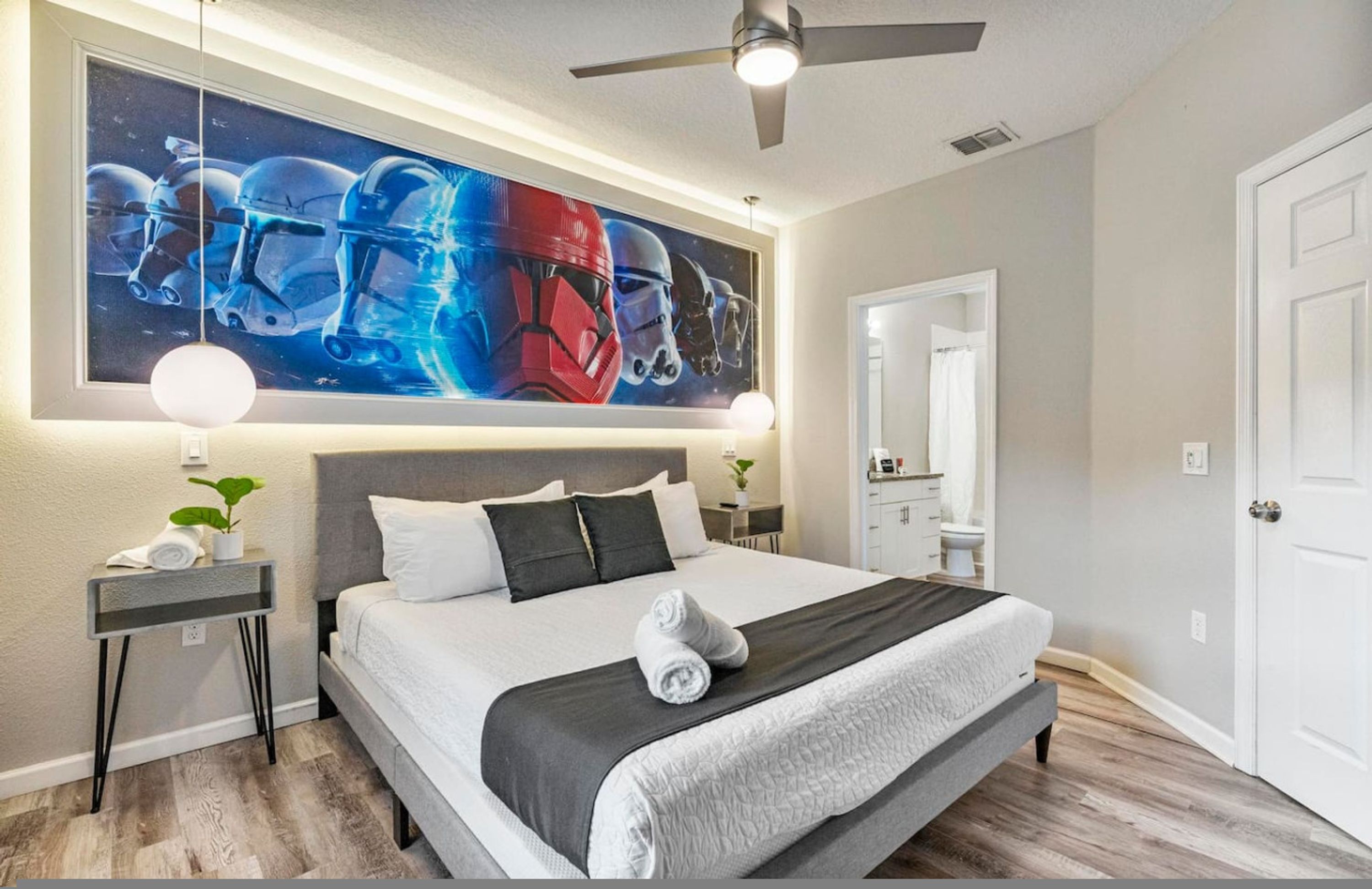 Un dormitorio con una cama grande, ventilador de techo, un cuadro en la pared, mesitas de noche y un espejo.