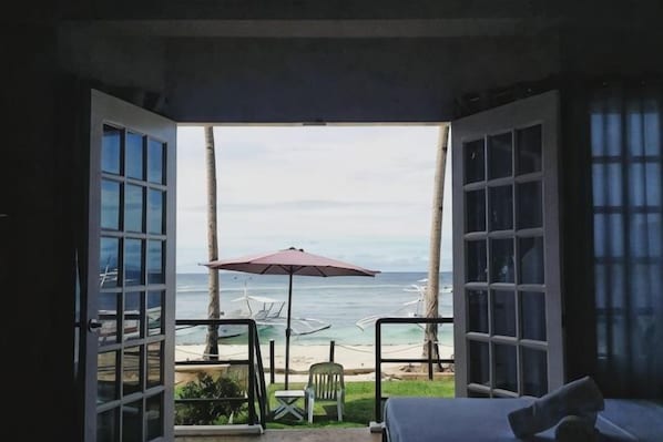 An open room with a view of the sea, a bed, a chair, and a table with an umbrella.