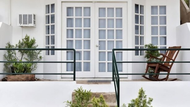 Un bâtiment blanc avec une grande porte à deux battants, un petit climatiseur et une chaise à bascule en bois.