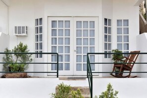 A white building with a large double door, a small air conditioning unit, and a wooden rocking chair. - Blue Ocean Bohol Beachfront (Panglao Municipality)