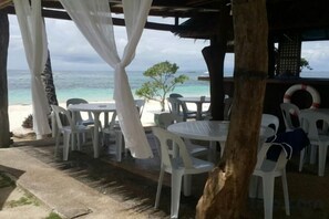 An outdoor seating area with tables and chairs, overlooking a beach and the ocean.