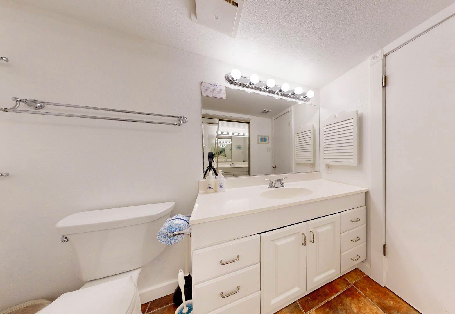 A modern bathroom with a white toilet, a vanity with a sink, and a large mirror.