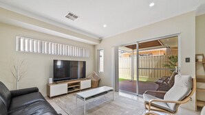 Una sala de estar moderna con una televisión de pantalla plana, un sofá, una mesa de centro y un ventanal corredero que da a un patio exterior.