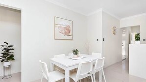 Un comedor moderno con una mesa y sillas blancas, una planta en maceta y un cuadro en la pared.