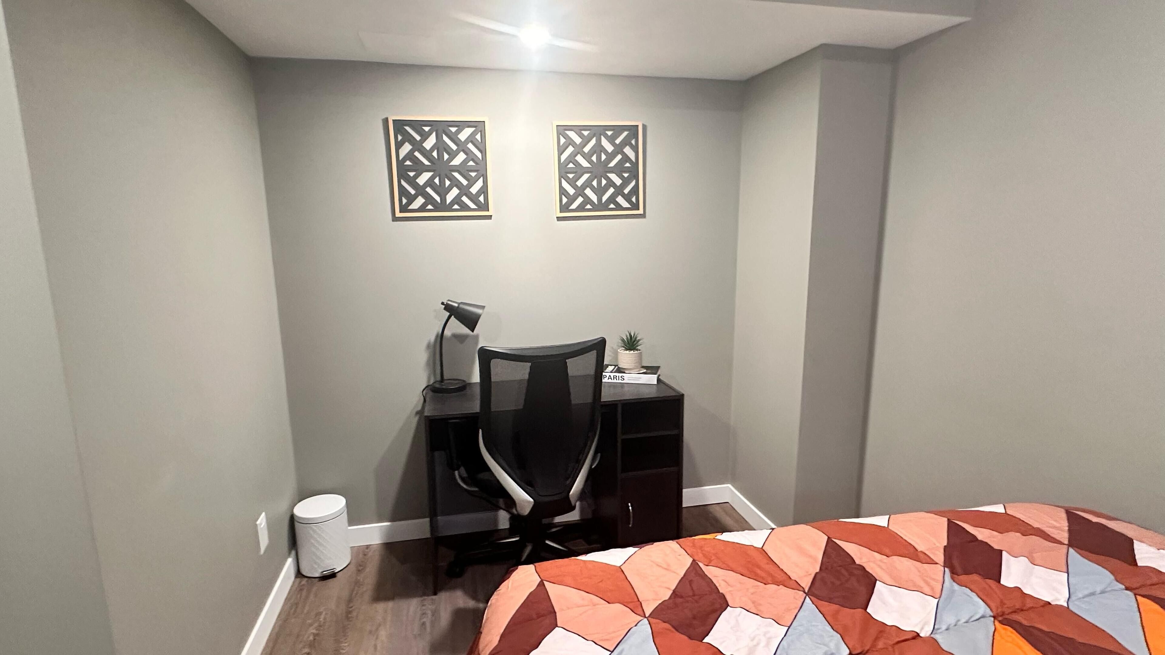 Un dormitorio pequeño y ordenado, con escritorio, silla y cama con una colcha de estampado geométrico.