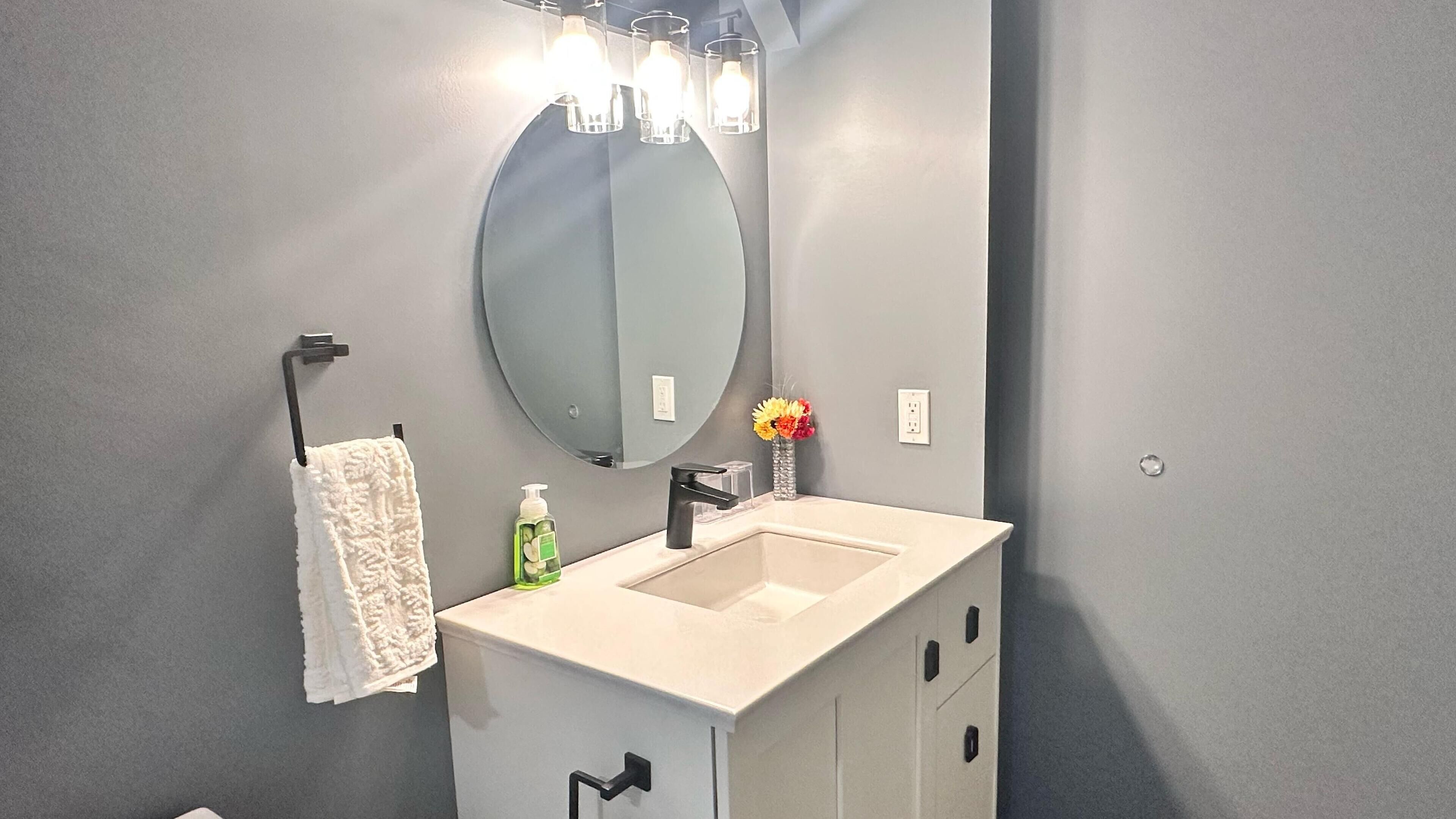 Un baño moderno con un tocador blanco, un espejo redondo y un perchero para toallas.