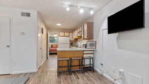 A modern kitchen with a central island, bar stools, and a flat-screen TV mounted on the wall. - The Ward - Resort Style Gameday Condo (Tallahassee)