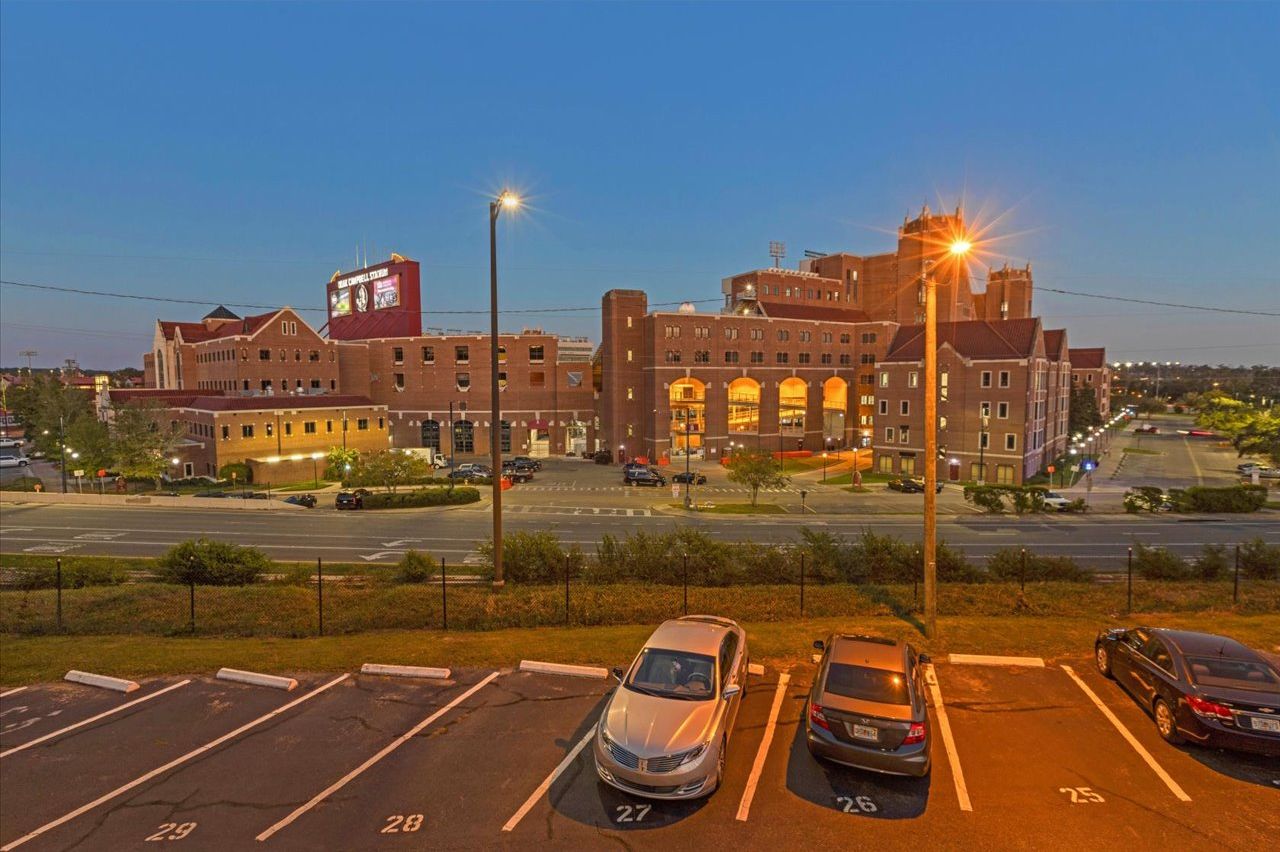 A parking lot with marked spaces and a large building with multiple floors and a prominent sign.