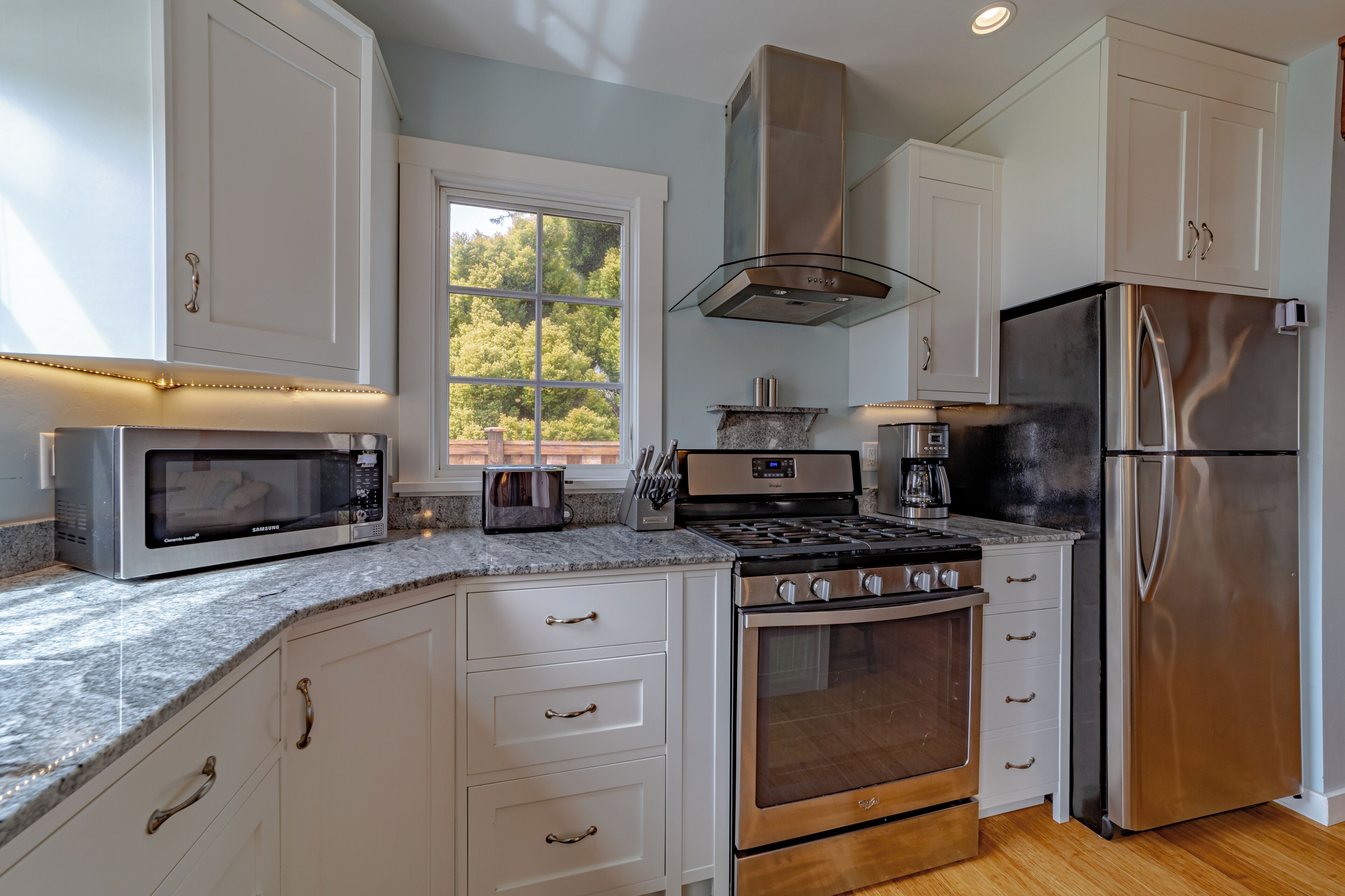 A modern kitchen with white cabinetry, stainless steel appliances, and a large window providing natural light.