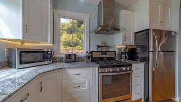 A modern kitchen with white cabinetry, stainless steel appliances, and a large window providing natural light.